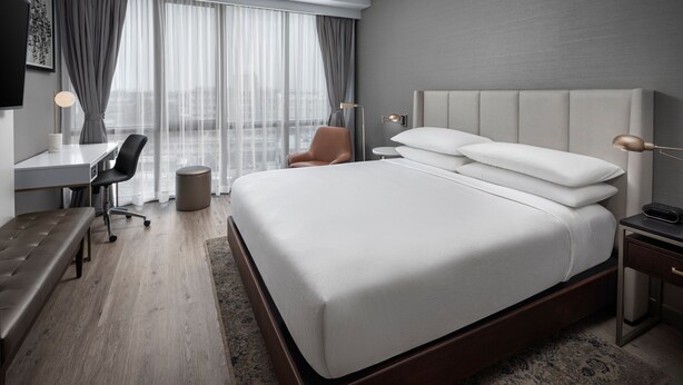 A modern hotel room with a large bed, a desk, a chair, and a view of the city through sheer curtains. - Four Points by Sheraton Flushing (Flushing)