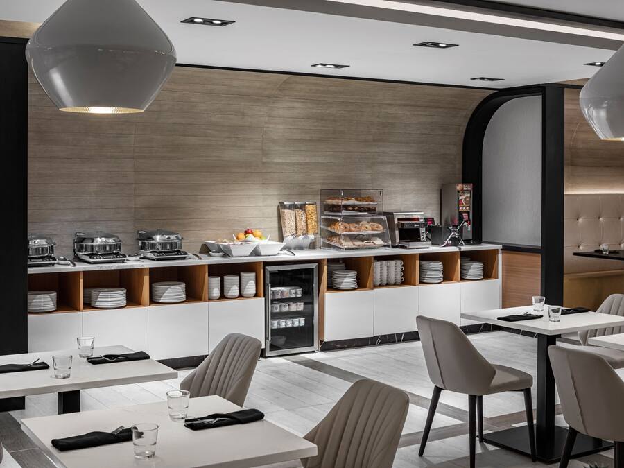 A modern restaurant with white tables and chairs, a counter with food displays, and a refrigerator.