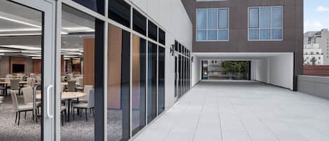A modern building exterior with a glass facade, a flat roof terrace, and a dining area visible through the glass.