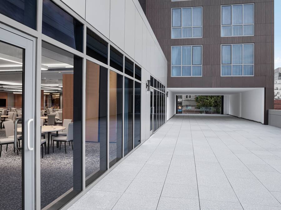 A modern building exterior with a glass facade, a flat roof terrace, and a dining area visible through the glass.