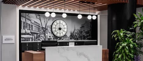Un mostrador de recepción con un reloj grande, el logotipo de Marriott Bonvoy y una planta en maceta.