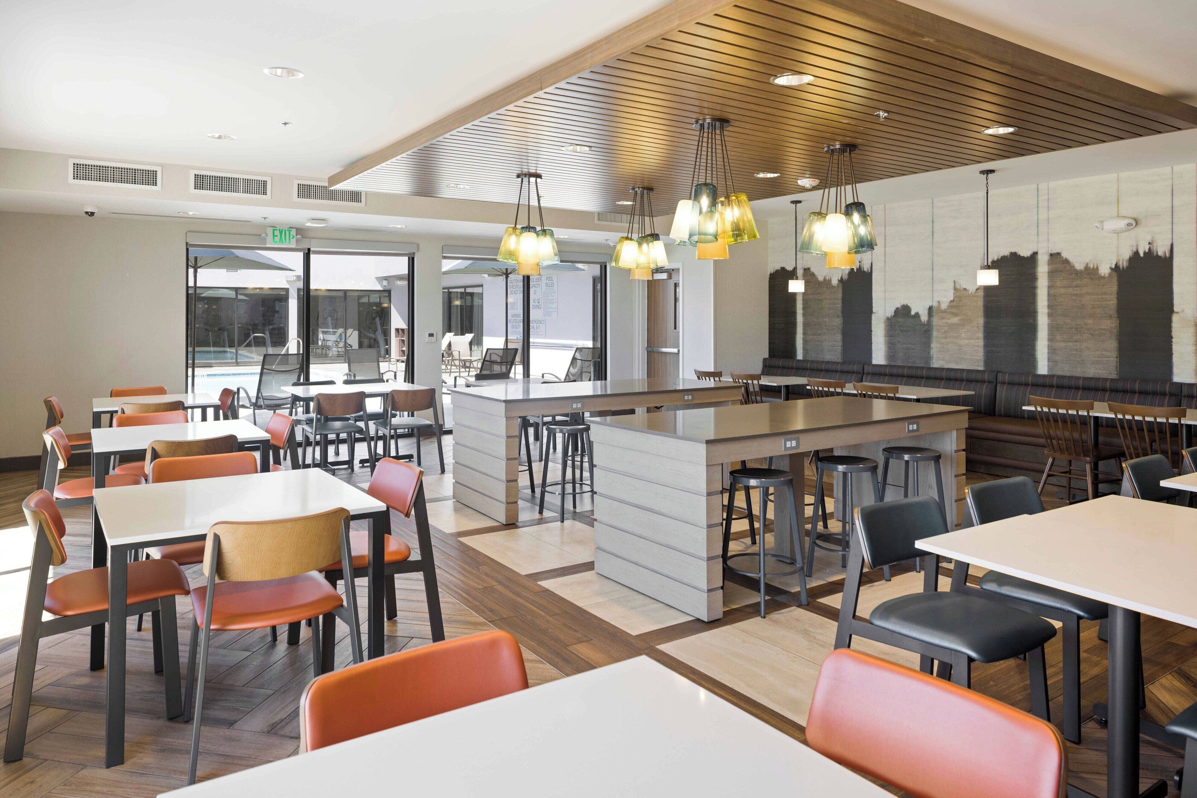 Un comedor moderno con varias mesas y sillas, una isla central con taburetes e iluminación colgante.