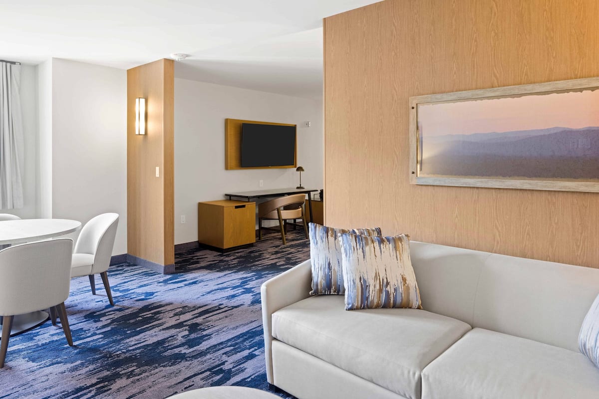 A hotel room with a white sofa, a desk with a computer, a flat-screen TV, and a painting on the wall.