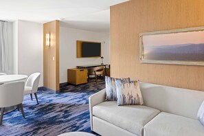 A hotel room with a white sofa, a desk with a computer, a flat-screen TV, and a painting on the wall. - Fairfield Inn & Suites by Marriott San Diego Pacific Beach (San Diego)