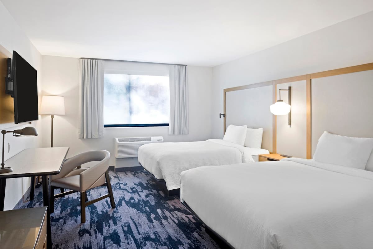 A hotel room with two beds, a desk with a chair, a TV, and a window with curtains.
