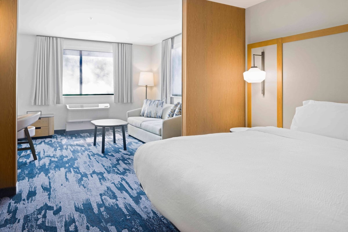 A hotel room with a large bed, a small round table, a sofa, a lamp, and a window with curtains.