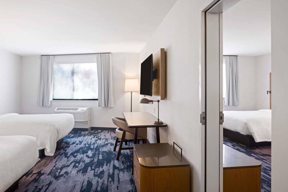 Habitación de hotel con dos camas, un escritorio, una silla, un televisor y una ventana con cortinas.