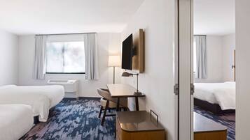 A hotel room with two beds, a desk, a chair, a TV, and a window with curtains.