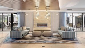 Una sala de estar moderna con chimenea de piedra, dos sofás, otomanas y una alfombra estampada.