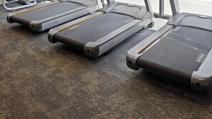 Gimnasio con cintas de correr, bicicletas estáticas y una zona de piscina visible a través de puertas de vidrio.