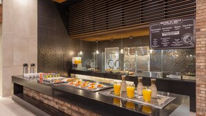 A breakfast buffet with various food items and beverages, a menu board listing ingredients, and a modern interior design with brick accents and wooden slats. - Four Points by Sheraton Monterrey Airport (Apodaca)