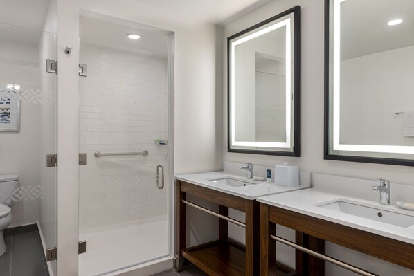 Un baño moderno con cabina de ducha de vidrio, dos lavabos con mueble de madera y un espejo grande.