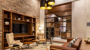 A modern living room with a brick wall, wooden shelves, a flat-screen TV, leather sofas, and a coffee table. - Four Points by Sheraton Monterrey Airport (Apodaca)