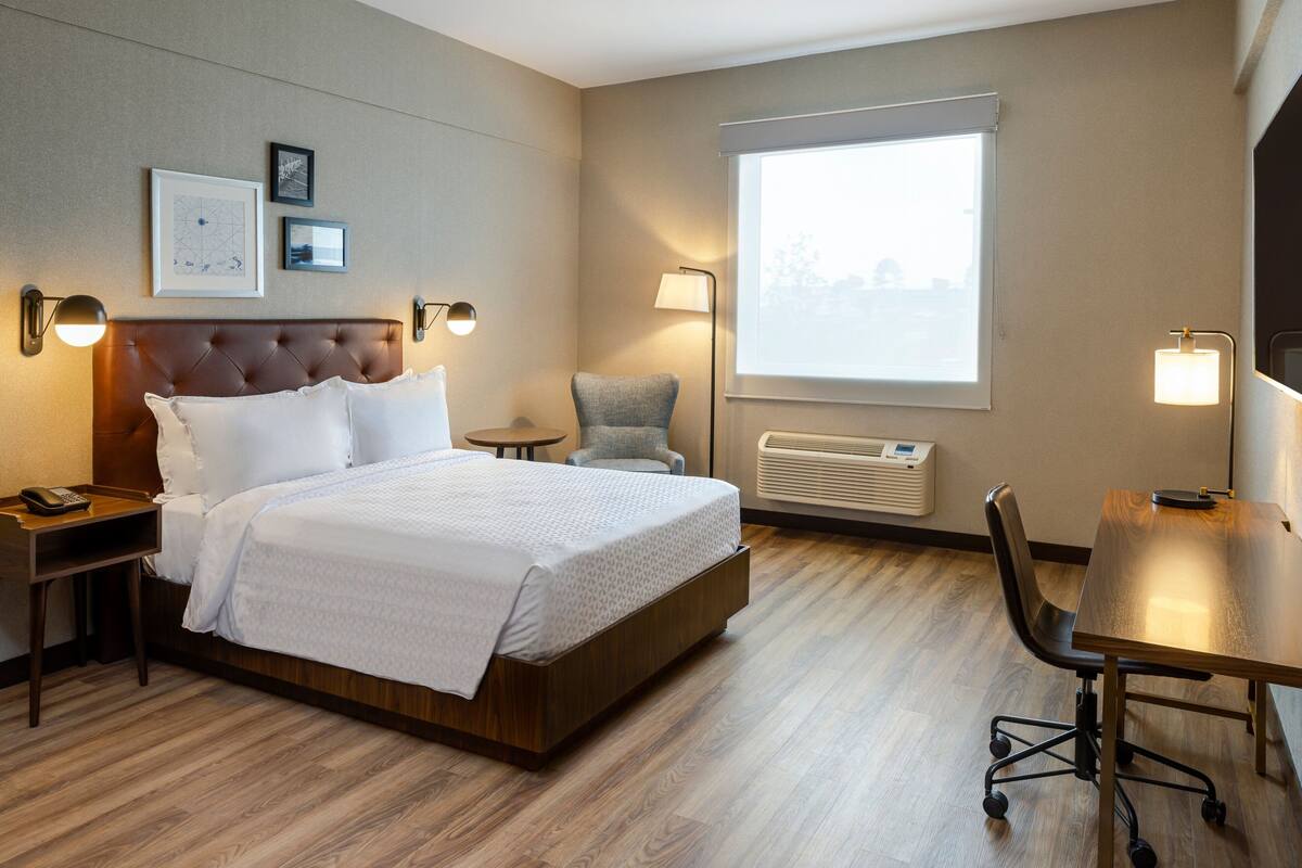 Een hotelkamer met een bed, nachtkastjes, een bureau, een stoel, een lamp en een raam met jaloezieën.