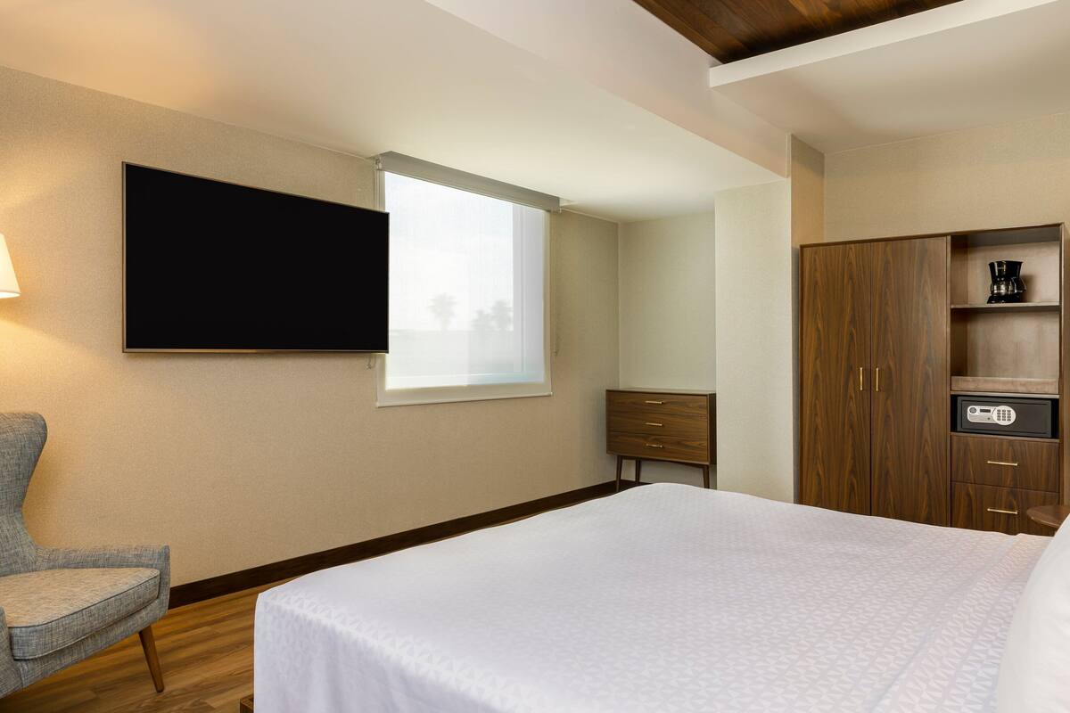 Een hotelkamer met een bed, een stoel, een televisie, een kledingkast en een raam.