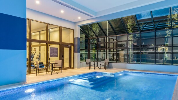 An indoor swimming pool with seating areas and large windows. - Four Points by Sheraton Monterrey Airport (Apodaca)