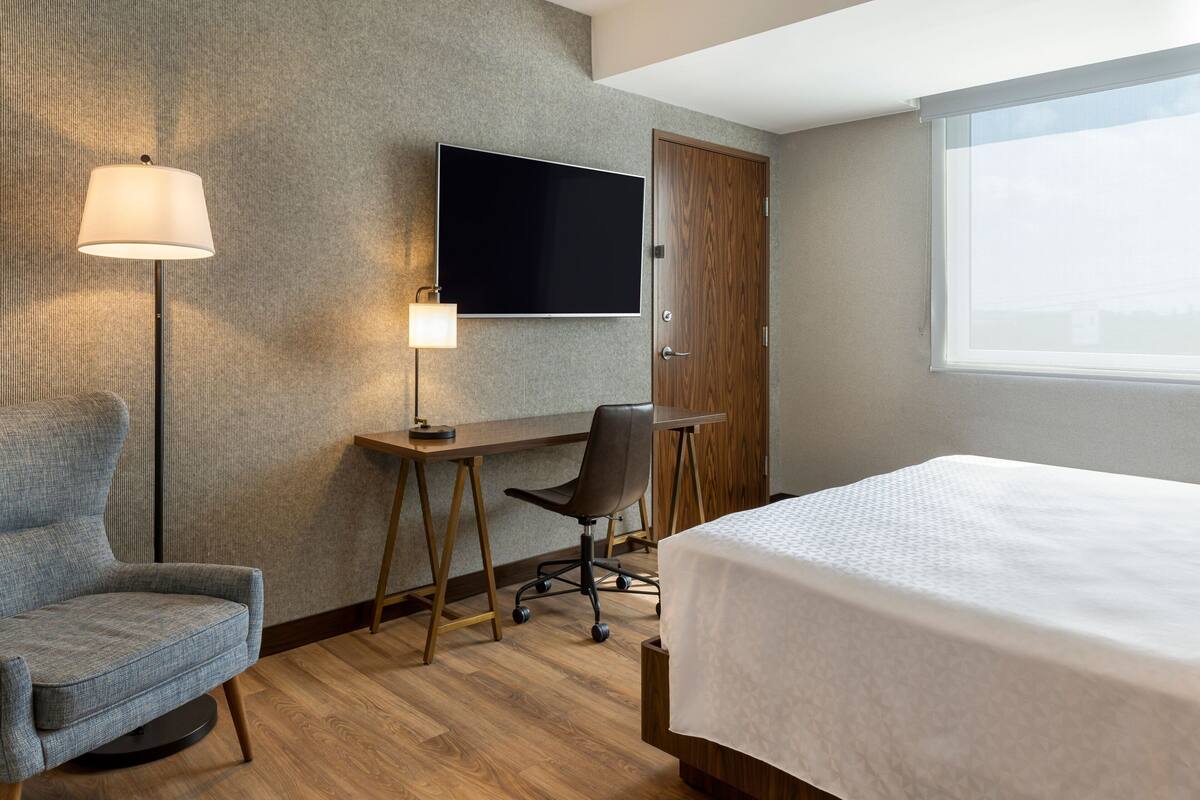 Een hotelkamer met een bed, een bureau met stoel, een televisie en een lamp.