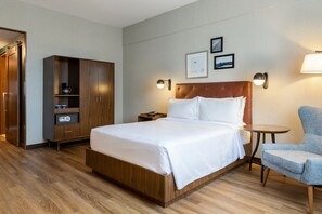 Une chambre d’hôtel avec un lit en bois, une armoire, une table de chevet avec une lampe et une petite table ronde.