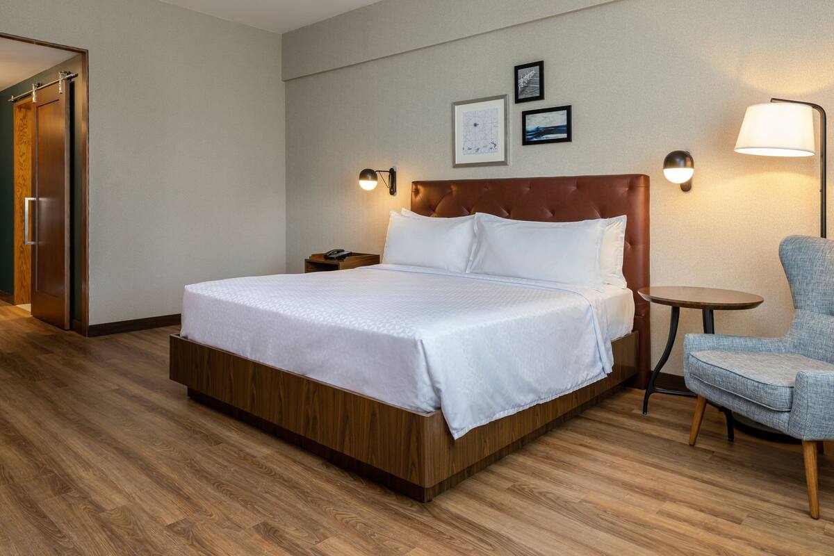 Een hotelkamer met een groot bed, een stoel, een klein tafeltje en een nachtkastje met een telefoon.