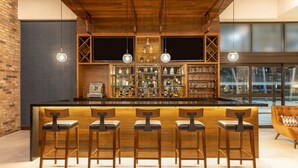 A bar area with a long counter, multiple stools, and shelves with bottles. - Four Points by Sheraton Monterrey Airport (Apodaca)