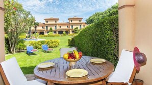 A round wooden table with four white chairs, a bowl of fruit, and plates and cutlery. - Port Pals Village by Interhome (Pals)