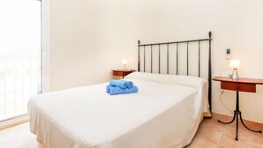 A hotel room with a bed, two bedside tables with lamps, a window, and a view of buildings outside. - Port Pals Village by Interhome (Pals)