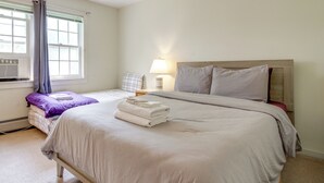 A hotel room with a bed, a bedside table with a lamp, a window with curtains, and a radiator. - Chic Dover Home w/ Hot Tub: 1 Mi to Golf! (West Dover)