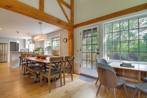 Une cuisine spacieuse avec des poutres en bois, un coin repas avec une table et des chaises en bois, et de grandes fenêtres offrant une vue sur l’extérieur.