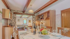 Comedor con pared de piedra, vigas de madera y una mesa para cuatro, con platos, vasos y un frutero.