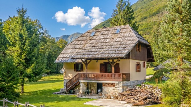 Una casa rústica de madera con balcón, cimientos de piedra y chimenea de piedra.