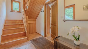 Una escalera de madera que sube a un segundo piso, una puerta con ventanal y una orquídea en maceta sobre una consola.