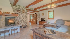 Amplia sala de estar con chimenea de piedra, vigas de madera, un sofá y un tablero de ajedrez.