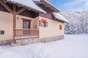 A wooden chalet with a stone foundation, wooden balcony, and a snow-covered roof.