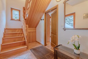 A wooden staircase leading to a second floor, a door with a view of snow-covered trees, and a potted orchid on a console table.