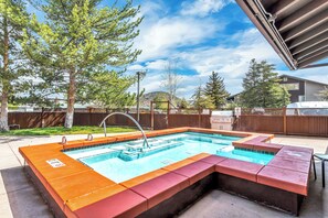 Ein rechteckiger Außenpool mit einem Whirlpoolbereich, umgeben von einer Holzterrasse und einem Metallzaun.
