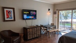 Quarto com escrivaninha de madeira, televisão na parede, poltrona de couro, cama e porta de vidro deslizante para área externa.