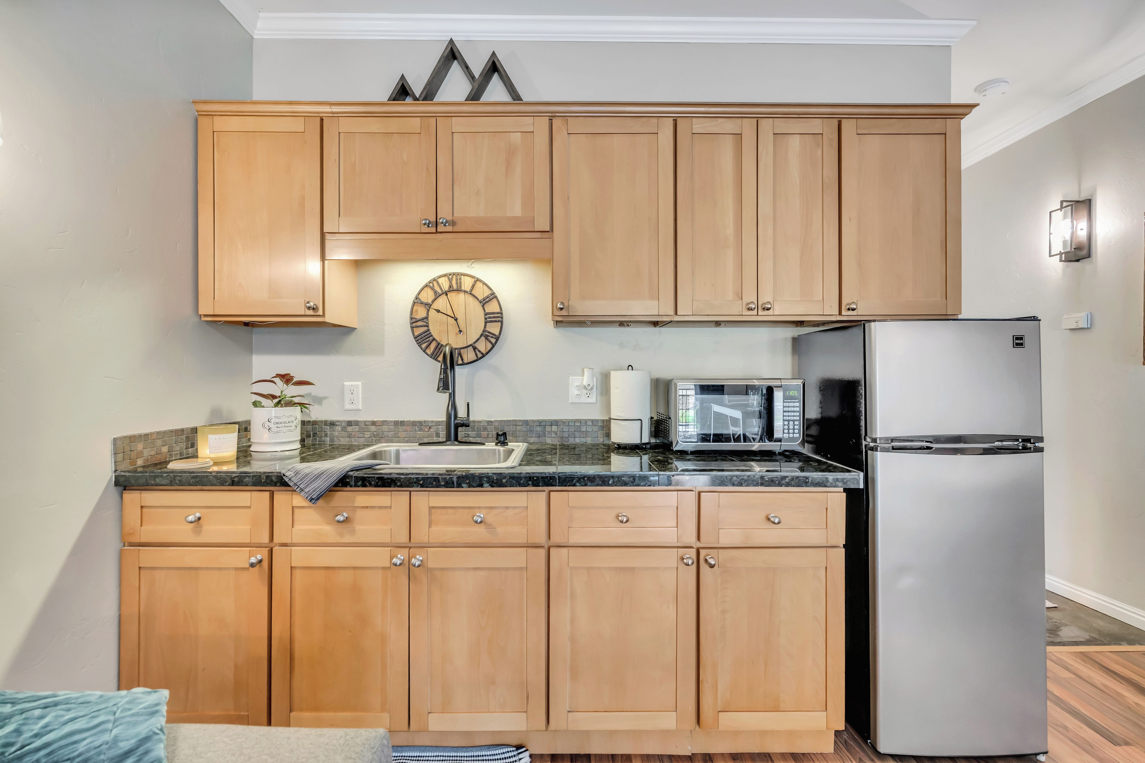 A kitchen with wooden cabinets, a stainless steel refrigerator, a microwave, and a clock.