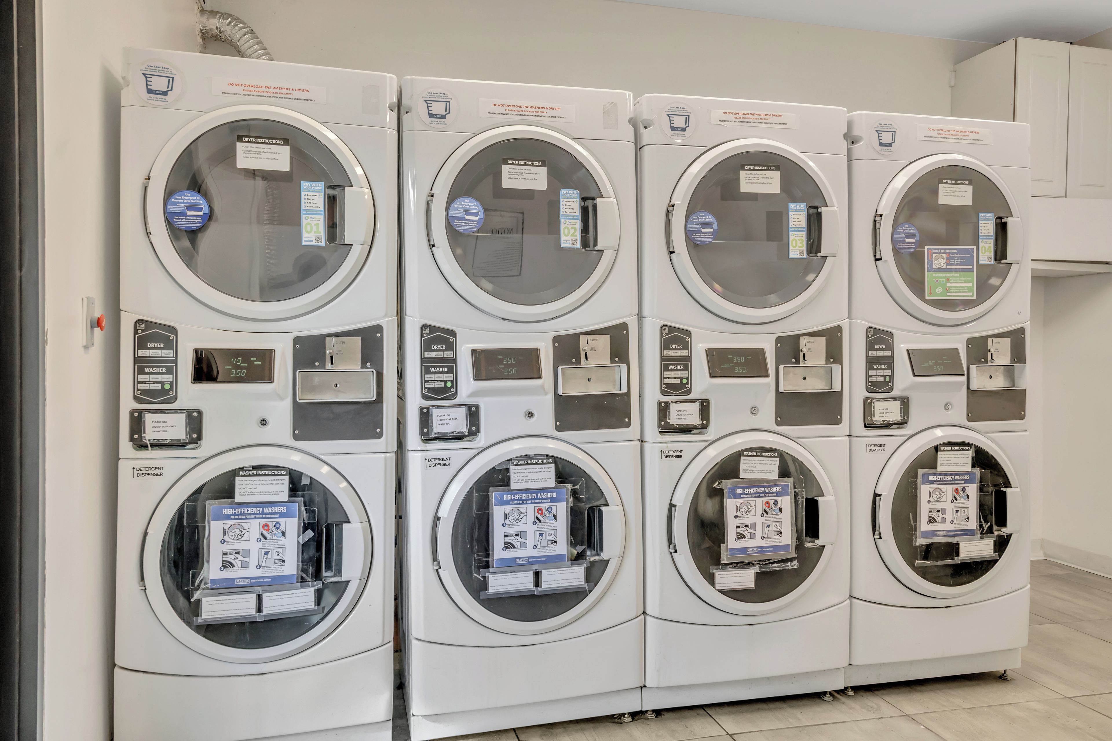 A row of four stacked laundry machines with control panels and detergent dispensers.