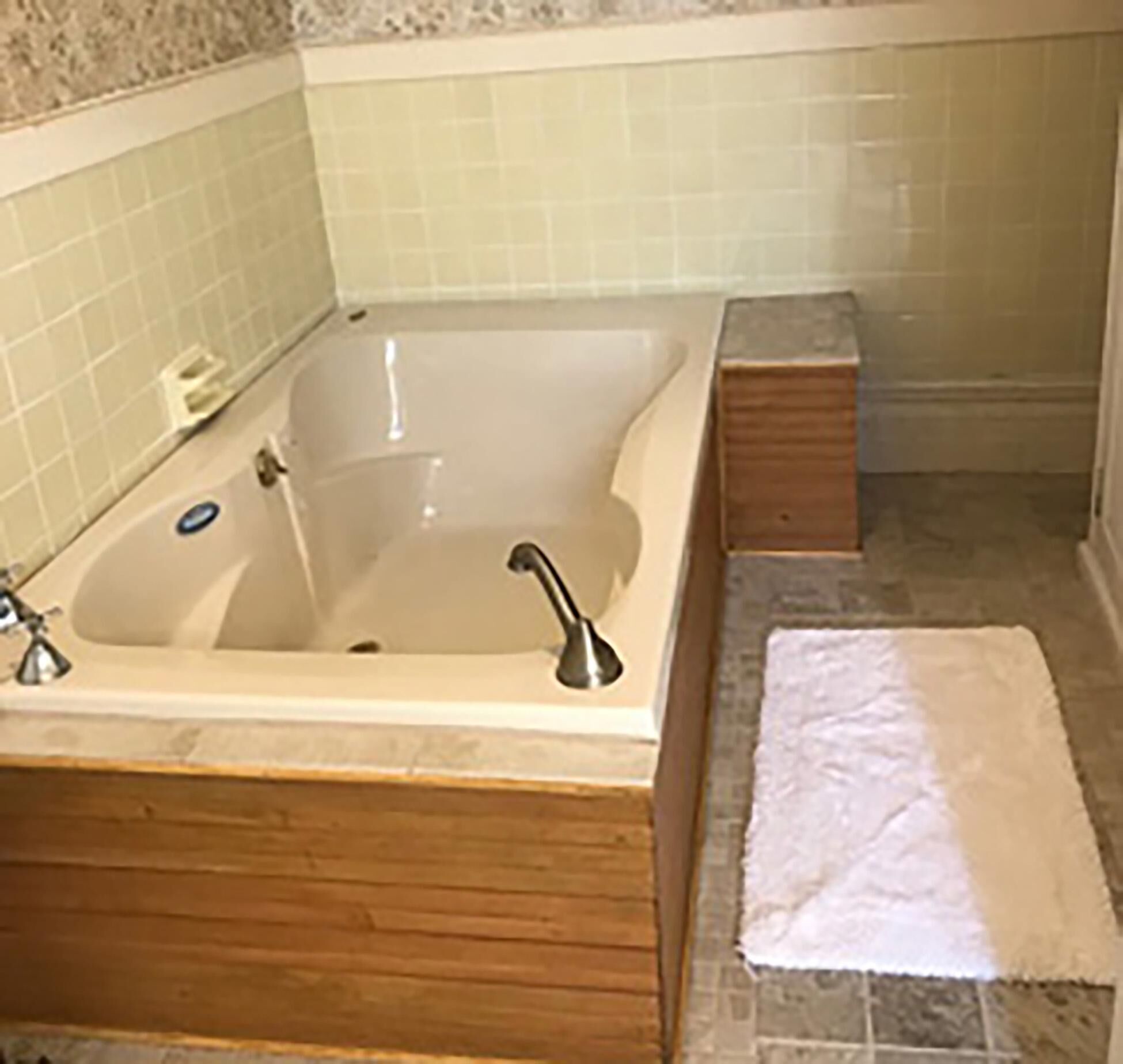 A bathroom with a bathtub, a wooden vanity, a towel, and a tiled wall.