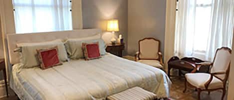 A bedroom with a large bed, a nightstand, a chair, and a window with curtains.
