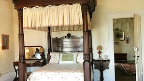 Een hemelbed met baldakijn, een nachtkastje met lamp en een bijzettafeltje met lamp.