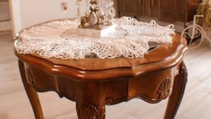 Een ronde houten tafel met een kantkleed en een glazen middelpunt.