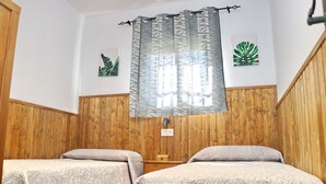 Une chambre avec deux lits, un lambris en bois, une fenêtre ornée d’un rideau à motifs et deux œuvres d’art accrochées au mur.