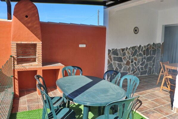 Un patio exterior con una parrilla de ladrillo, un muro de piedra y suelo de baldosas.