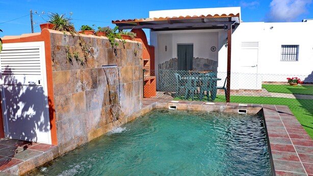 Une piscine avec un mur en pierre et une petite cascade décorative.