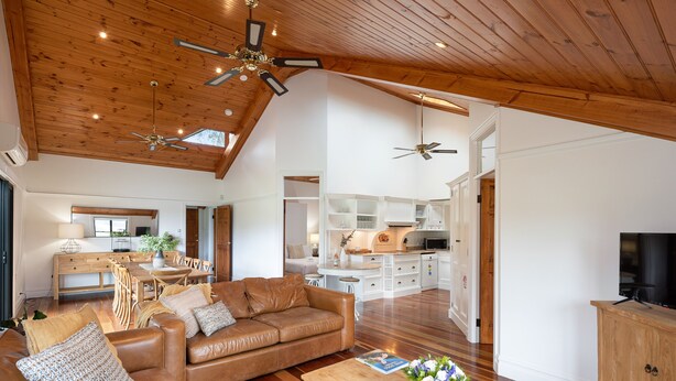 A spacious living room with a brown leather sofa, a wooden coffee table, and a ceiling fan. - Rustic charm amongst the vines in Pokolbin (Pokolbin)