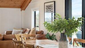 A dining area with a wooden table, chairs, a vase with green plants, a brown leather couch, and a framed artwork on the wall. - Rustic charm amongst the vines in Pokolbin (Pokolbin)