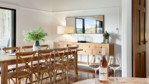 A dining area with a wooden table and chairs, a vase with flowers, and two wine glasses and bottles on the table. - Rustic charm amongst the vines in Pokolbin (Pokolbin)