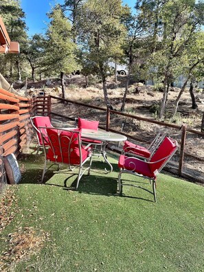 A patio area with a table and four red chairs, surrounded by a wooden fence and trees.