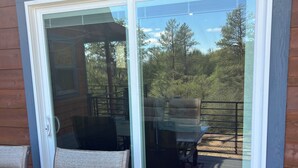 En terrasse med to stole og et bord, en skydedør samt udsigt over et skovområde.